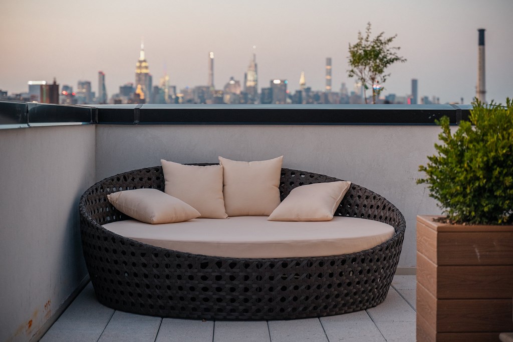 a round rattan sofa with pillows on a balcony overlooking a city